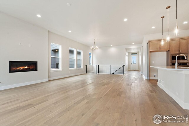 unfurnished living room with a chandelier, a glass covered fireplace, light wood-style flooring, visible vents, and recessed lighting