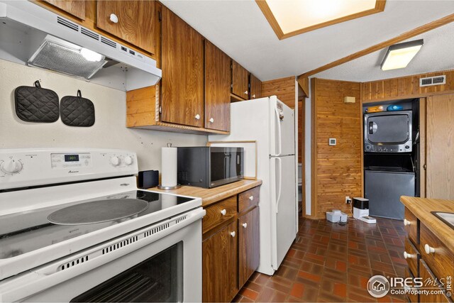 kitchen featuring under cabinet range hood, white electric stove, brown cabinetry, and stacked washer and dryer