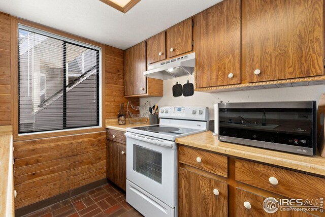 kitchen featuring brown cabinetry, wooden walls, white electric range, and under cabinet range hood