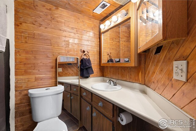 bathroom featuring visible vents, toilet, wood walls, and vanity