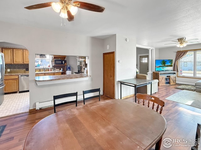 105 N Logan Ave, Haxtun, CO 80731 - dining room featuring a ceiling fan, a baseboard heating unit, light wood-type flooring, and arched walkways