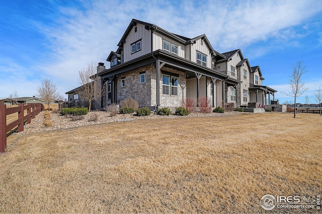 view of home's exterior featuring stone siding, fence, covered porch, board and batten siding, and a yard
