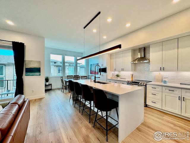kitchen featuring light countertops, a breakfast bar, a kitchen island with sink, stainless steel appliances, and wall chimney range hood