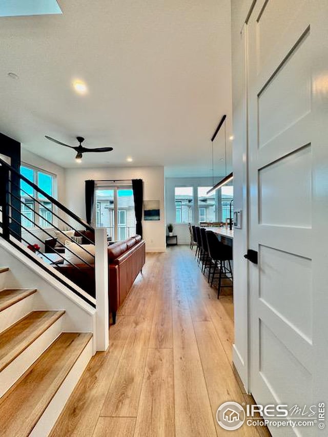 corridor with light wood-style flooring, baseboards, and stairs