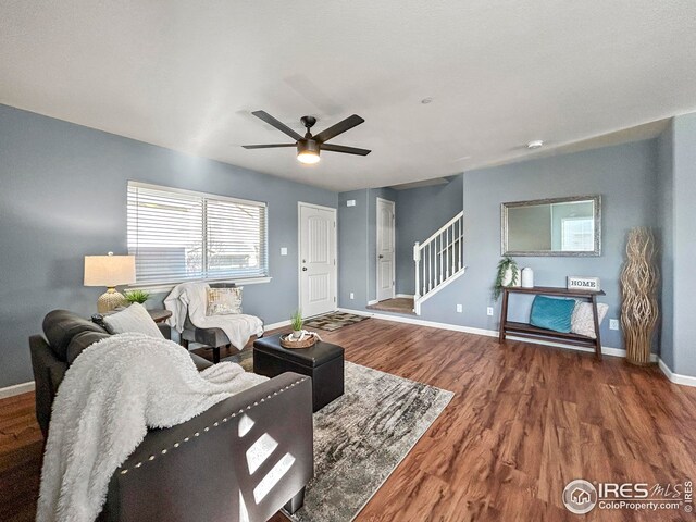 living area with baseboards, wood finished floors, ceiling fan, and stairway