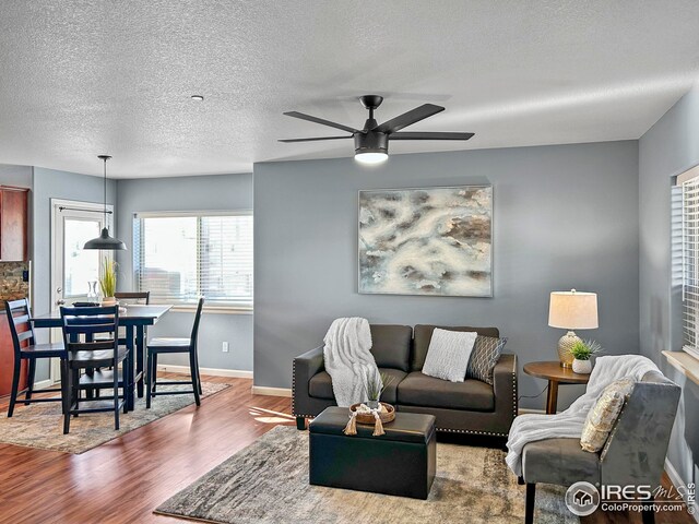 living area featuring baseboards, a textured ceiling, wood finished floors, and a ceiling fan
