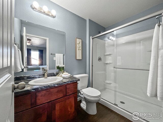 bathroom with toilet, vanity, a shower stall, wood finished floors, and a textured wall