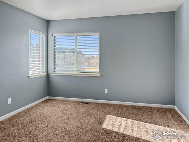 carpeted empty room featuring baseboards and visible vents
