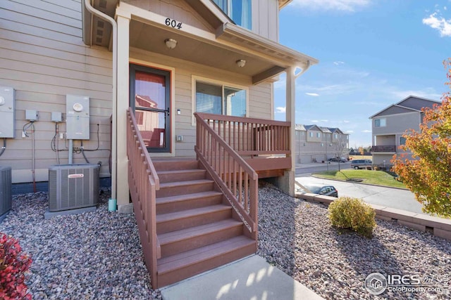 view of exterior entry featuring board and batten siding, a porch, central AC, and a residential view