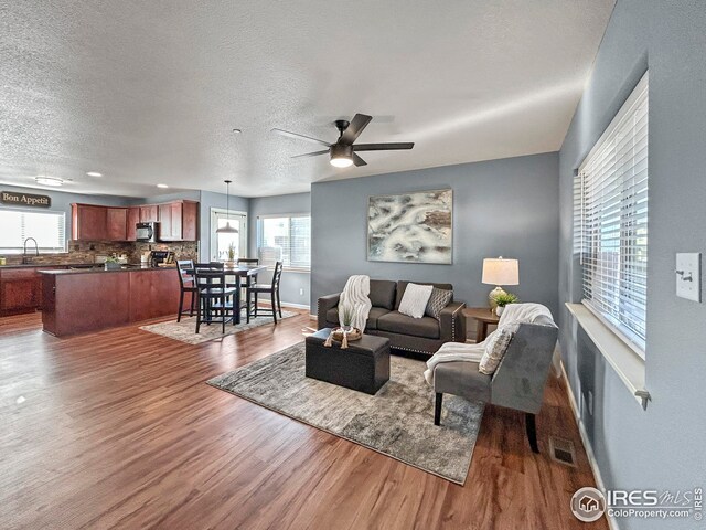 living area with baseboards, a textured ceiling, visible vents, a ceiling fan, and wood finished floors