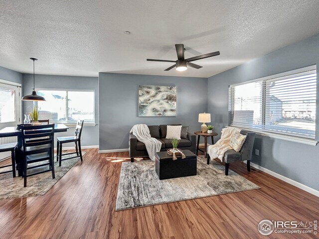 living area with baseboards, wood finished floors, ceiling fan, and a textured ceiling