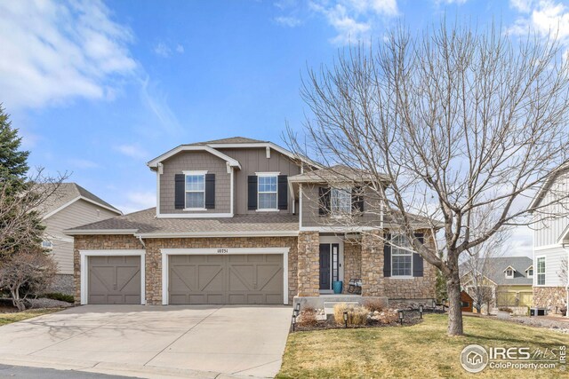 view of front of property featuring stone siding, driveway, an attached garage, and a front lawn