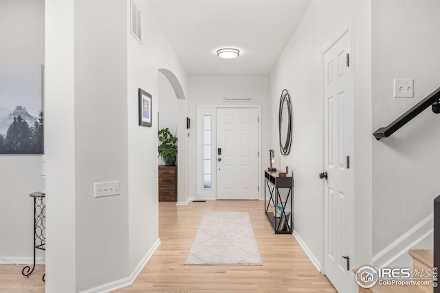 entrance foyer with baseboards, arched walkways, visible vents, and light wood finished floors