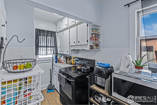 919 State St, Fort Morgan, CO 80701 - kitchen featuring black electric range, stainless steel microwave, white cabinetry, light wood-type flooring, and light countertops