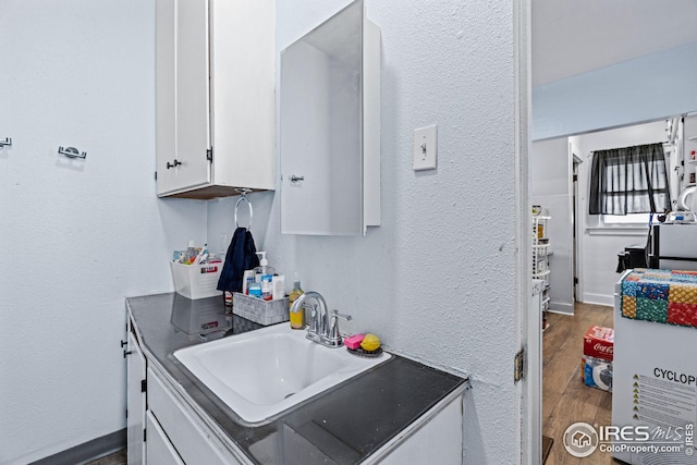 919 State St, Fort Morgan, CO 80701 - kitchen featuring white cabinetry, a sink, wood finished floors, a textured wall, and baseboards