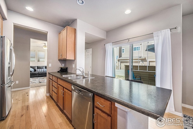 kitchen featuring a sink, appliances with stainless steel finishes, a peninsula, light wood-type flooring, and dark countertops