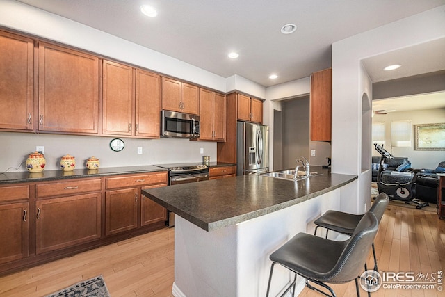 kitchen featuring a sink, a kitchen bar, stainless steel appliances, dark countertops, and light wood-style floors