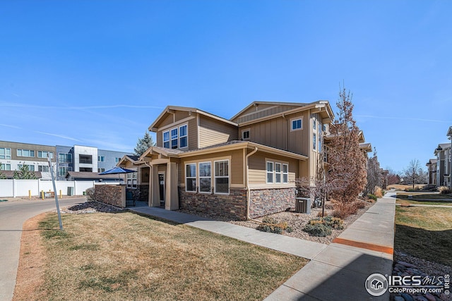 craftsman house featuring stone siding, fence, central AC, a front yard, and board and batten siding