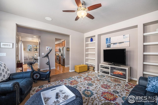 living room with a textured ceiling, baseboards, ceiling fan, and built in shelves