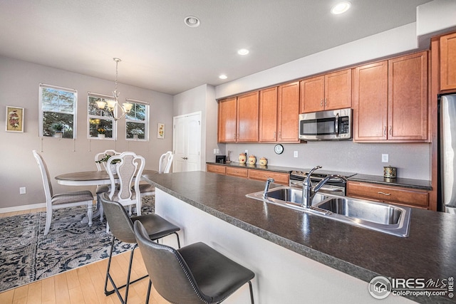 kitchen featuring brown cabinets, dark countertops, appliances with stainless steel finishes, a sink, and a notable chandelier