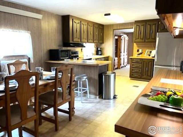 kitchen with light countertops, a peninsula, light floors, black microwave, and freestanding refrigerator