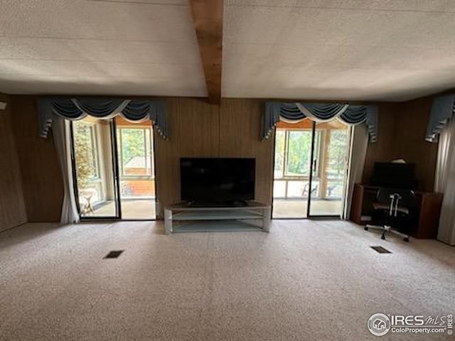 unfurnished living room featuring carpet flooring, plenty of natural light, wood walls, and beamed ceiling