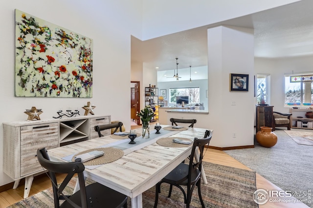 dining area featuring baseboards, a towering ceiling, a healthy amount of sunlight, and light wood-type flooring
