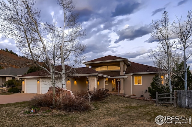 view of front of house with stucco siding, roof with shingles, fence, driveway, and a garage