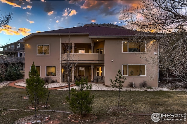 back of house at dusk featuring stucco siding, a balcony, and a patio area