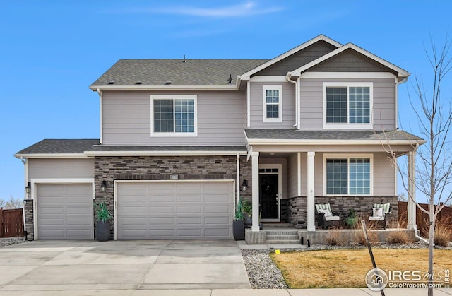 view of front of property featuring stone siding, fence, driveway, covered porch, and a shingled roof