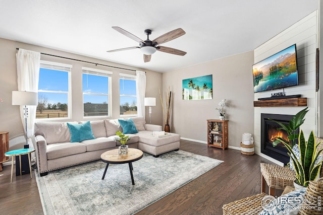 living room with a ceiling fan, dark wood-type flooring, baseboards, and a glass covered fireplace