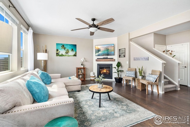 living room with wood finished floors, a glass covered fireplace, stairway, and a ceiling fan