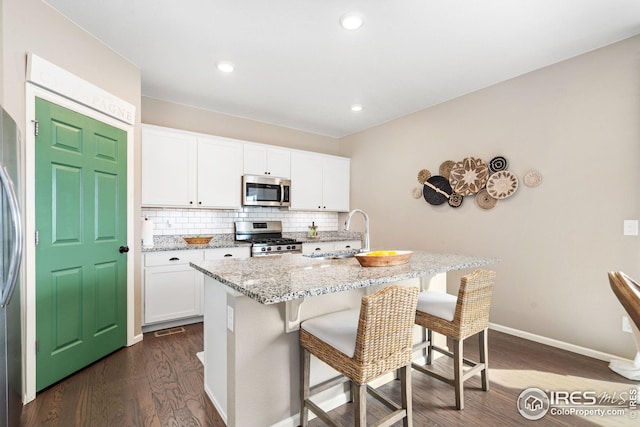 kitchen with dark wood-style flooring, a breakfast bar, appliances with stainless steel finishes, light stone counters, and backsplash