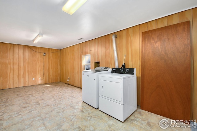 laundry room with washing machine and dryer, wood walls, and light flooring