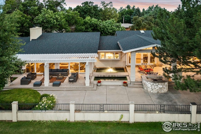 back of house with an outdoor living space with a fire pit, a shingled roof, a chimney, and fence