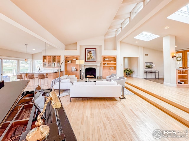 living room featuring light wood-type flooring, a skylight, high vaulted ceiling, a fireplace, and built in features