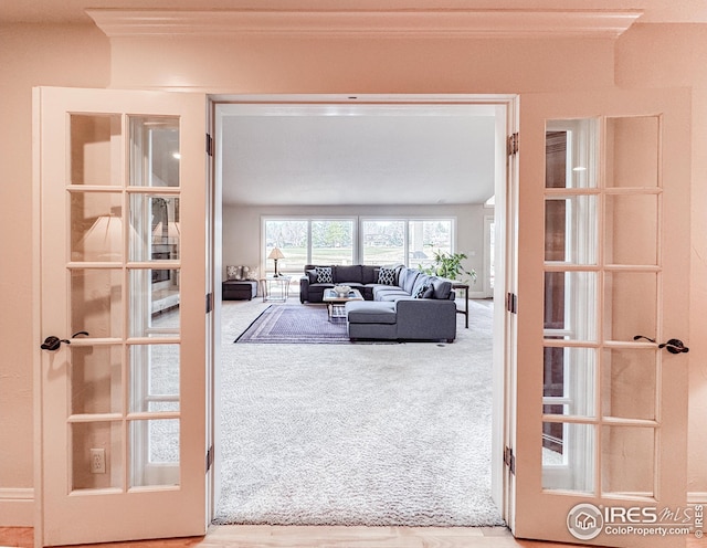 carpeted living area with ornamental molding and french doors