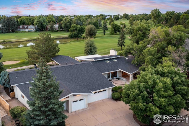 aerial view at dusk of a water view, view of wooded area, and view of golf course