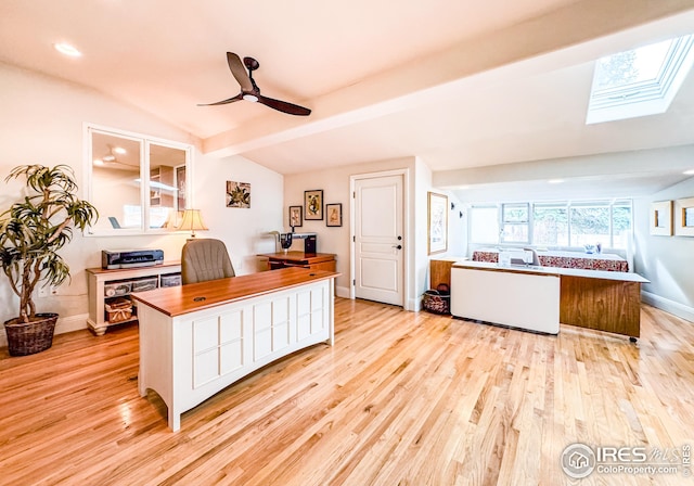 office area featuring vaulted ceiling, a skylight, light wood finished floors, ceiling fan, and baseboards