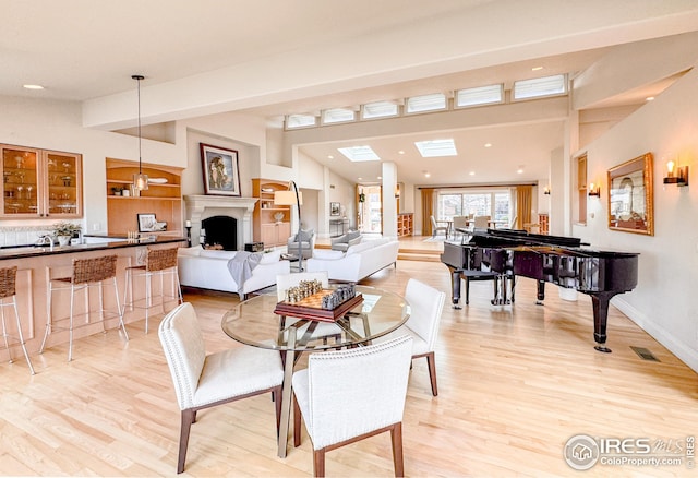 dining area featuring light wood-style flooring, a fireplace, baseboards, recessed lighting, and beamed ceiling