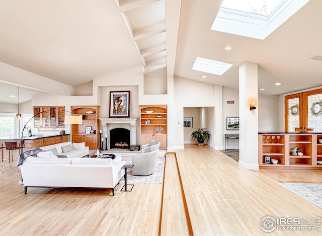 living room with a skylight, light wood finished floors, high vaulted ceiling, a fireplace with raised hearth, and baseboards