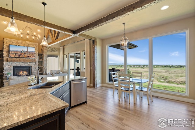 kitchen featuring dishwasher, a stone fireplace, a sink, baseboards, and a chandelier