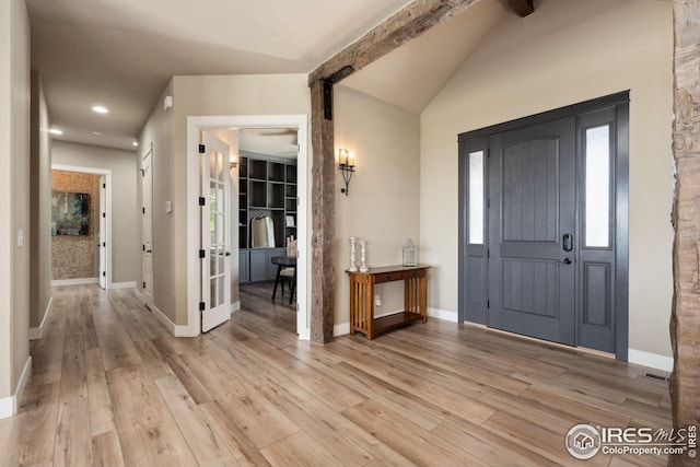 foyer featuring light wood-type flooring, vaulted ceiling with beams, baseboards, and visible vents