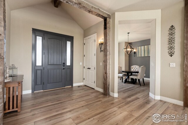 entryway with a chandelier, light wood-style floors, vaulted ceiling with beams, and baseboards