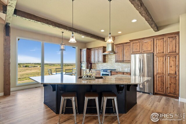 kitchen with wall chimney range hood, baseboards, stainless steel appliances, and beamed ceiling