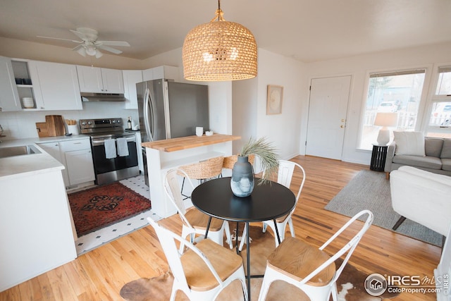 kitchen featuring ceiling fan with notable chandelier, hanging light fixtures, light wood-style flooring, under cabinet range hood, and electric stove