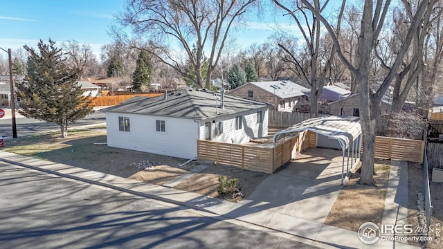 exterior space featuring fence, an outbuilding, a carport, a residential view, and driveway