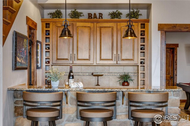 3865 Valley Crest Dr, Timnath, CO 80547 - kitchen featuring decorative light fixtures, light stone counters, brown cabinets, and a kitchen bar