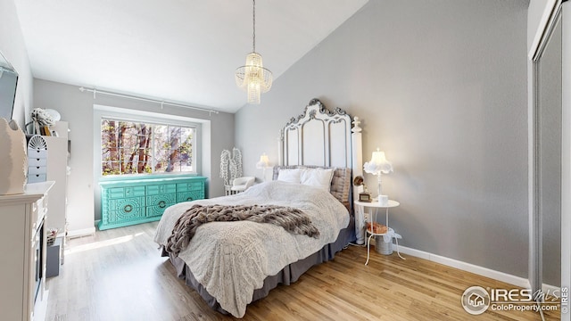 bedroom featuring baseboards, lofted ceiling, an inviting chandelier, and light wood-type flooring