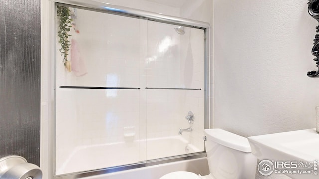 bathroom with a textured wall, toilet, and shower / bath combination with glass door